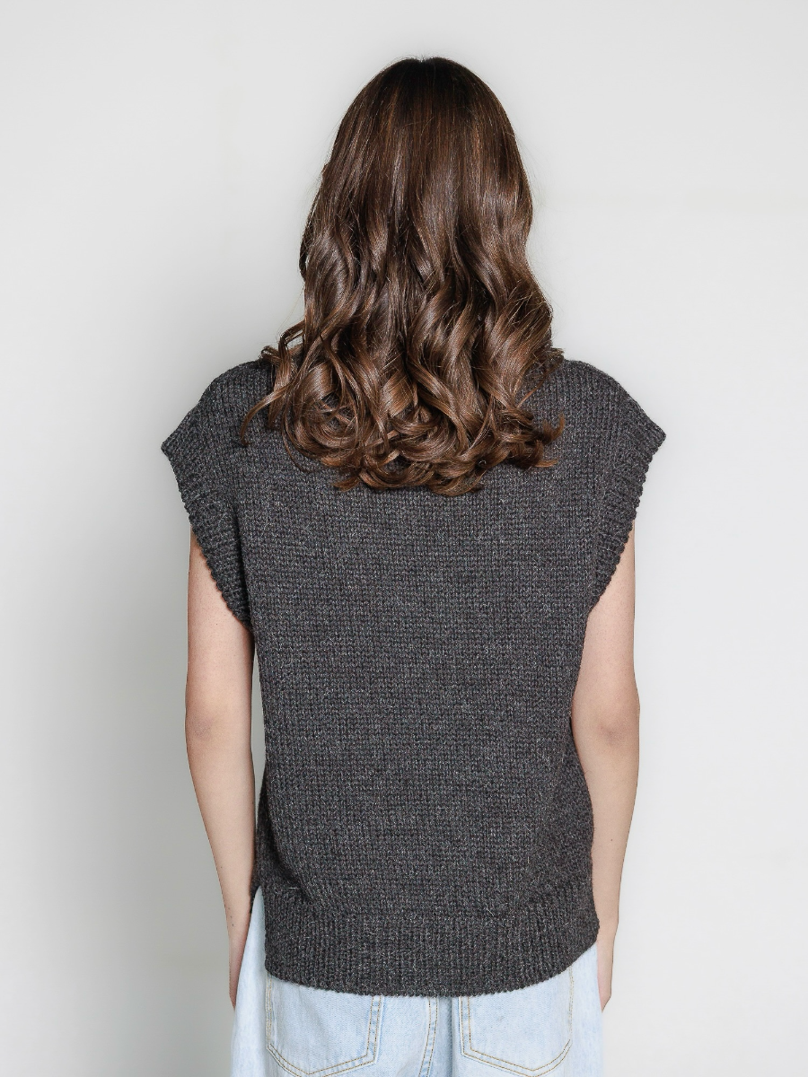 Woman wearing a grey knitted vest with blue jeans on a plain background