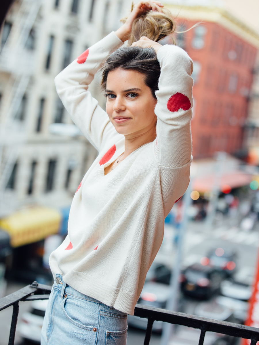 Woman wearing a white sweater with red heart patterns on a city street.