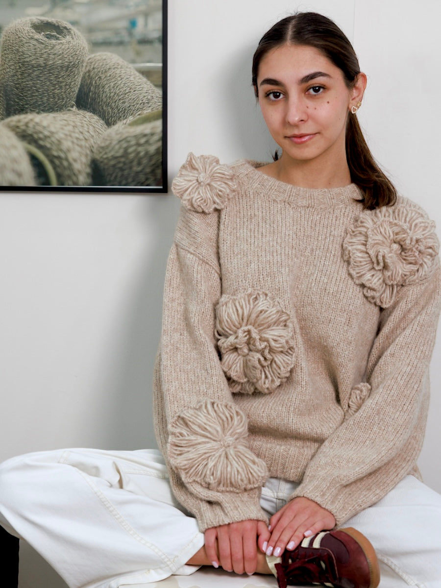 Woman wearing a beige sweater with floral embellisments sitting on a white couch.