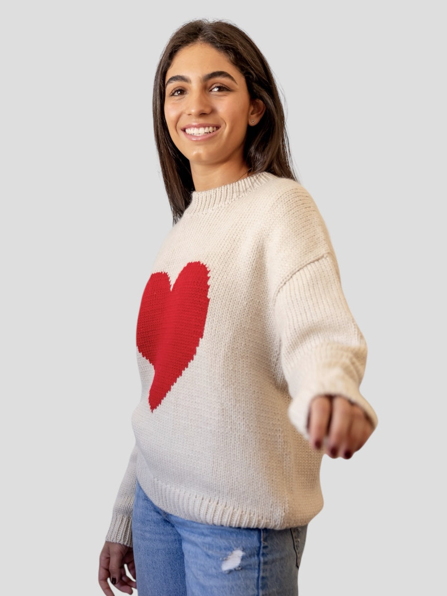 model wearing a white sweater with a red heart design against a plain background