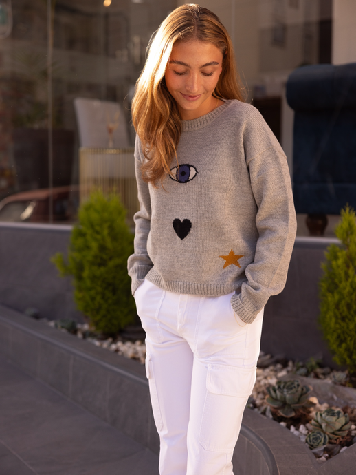 grey sweater decorated with a turkish eye, heart and a star on a model in city street