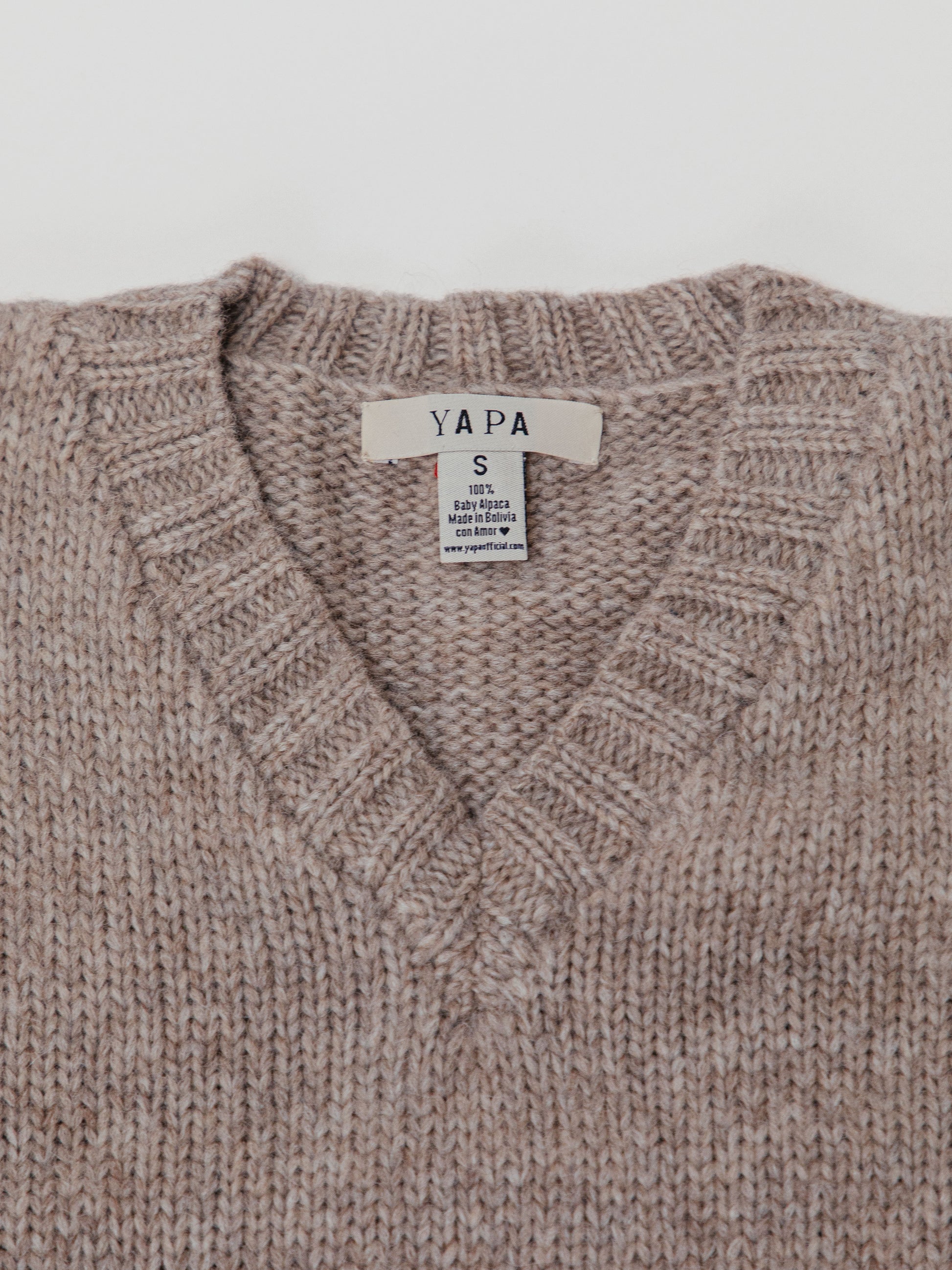Close-up of a brown knitted sweater with a 'YAPA' label on a white background