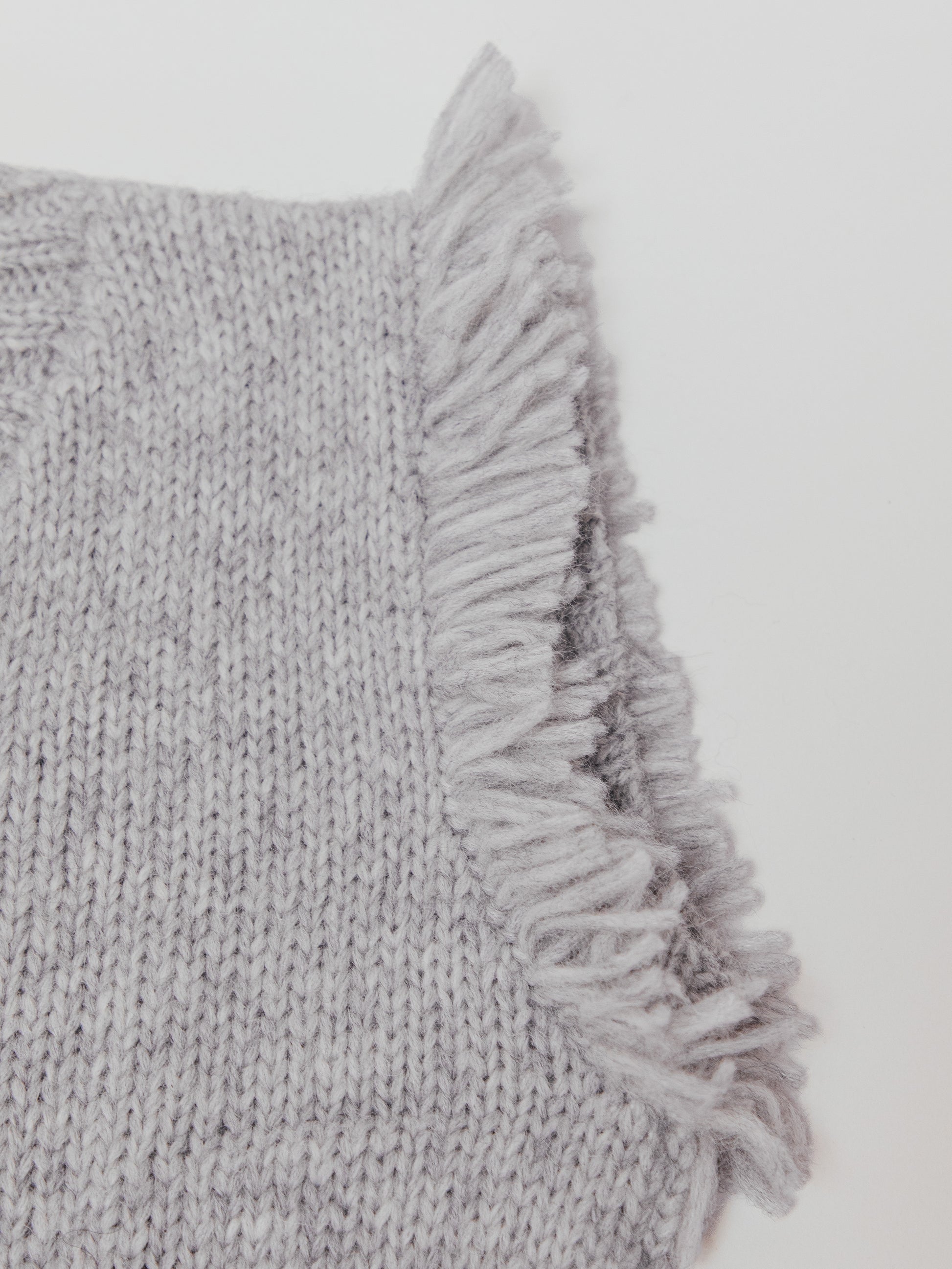 Gray knitted sweater vest with frayed edge on a light gray background