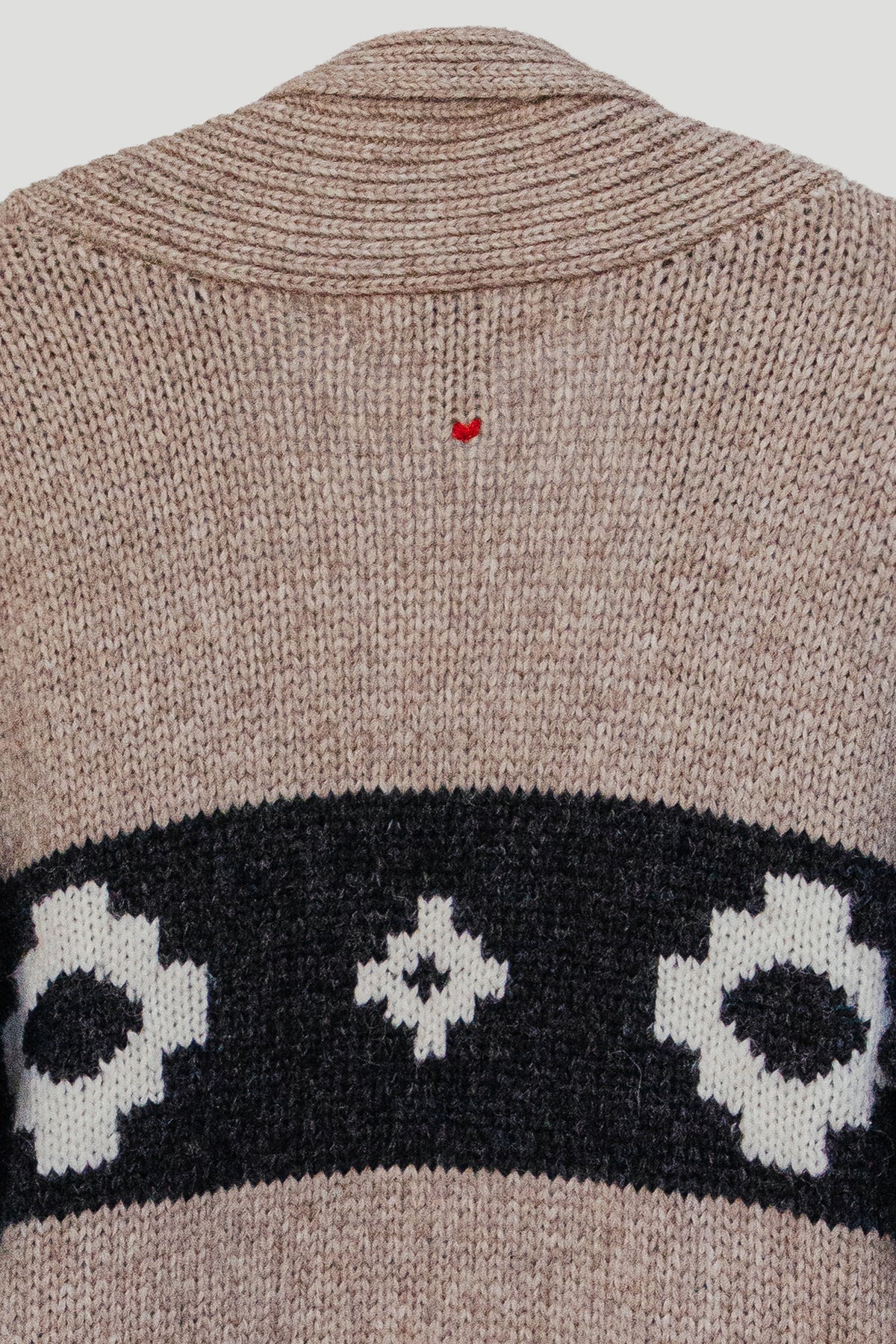 Close-up of a knit sweater back in heathered taupe with a wide black band featuring white geometric motifs and a small red embroidered heart near the neckline.