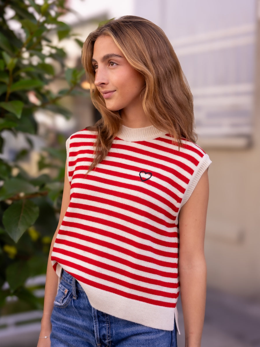 Woman wearing a black and white striped knitted vest over a white blouse with blue jeans on a city street background