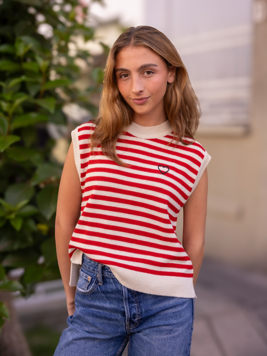 Woman wearing a black and white striped knitted vest over a white blouse with blue jeans on a city street background