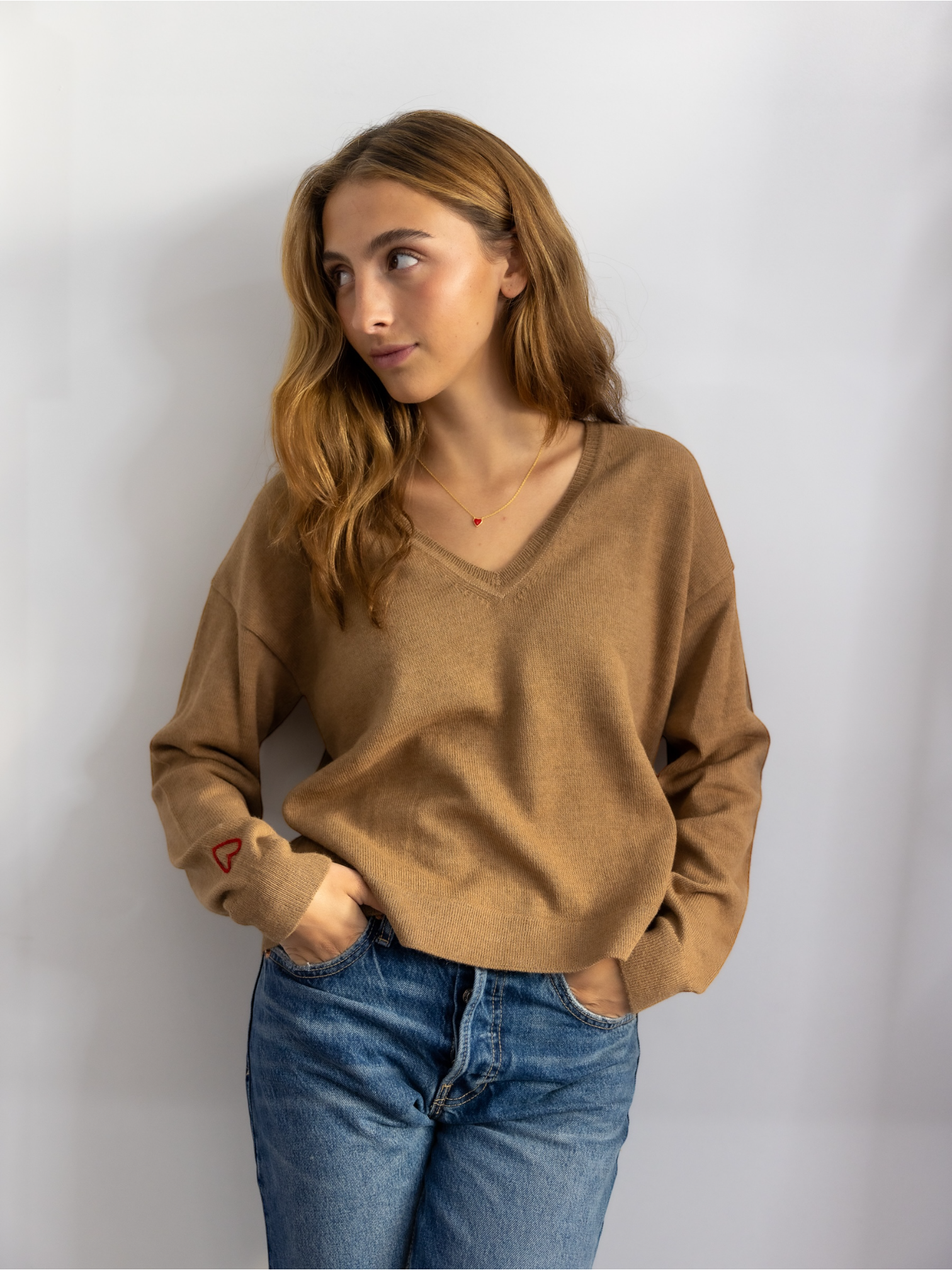 A woman wearing a beige V-neck alpaca wool sweater with long sleeves, paired with blue jeans.