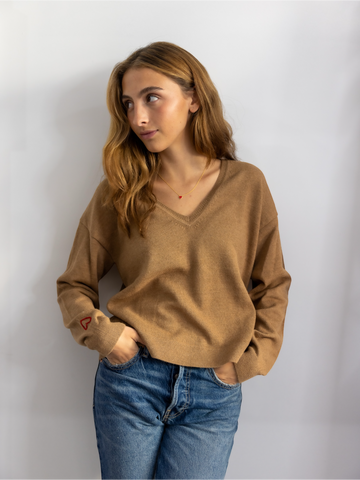 A woman wearing a beige V-neck alpaca wool sweater with long sleeves, paired with blue jeans.