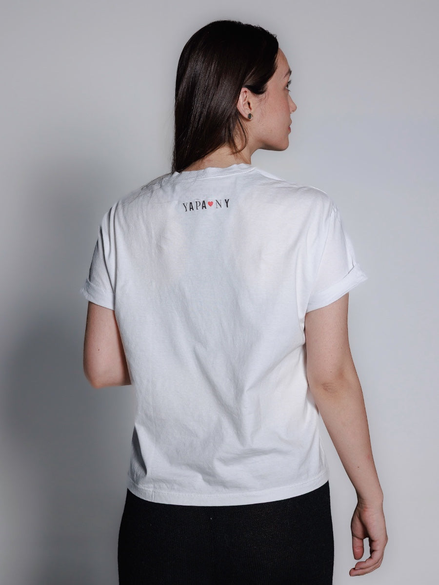 White cotton t-shirt featuring a minimalist embroidered New York City skyline with a small red heart and “NYC” lettering on the front, shown here on a model with a plain background