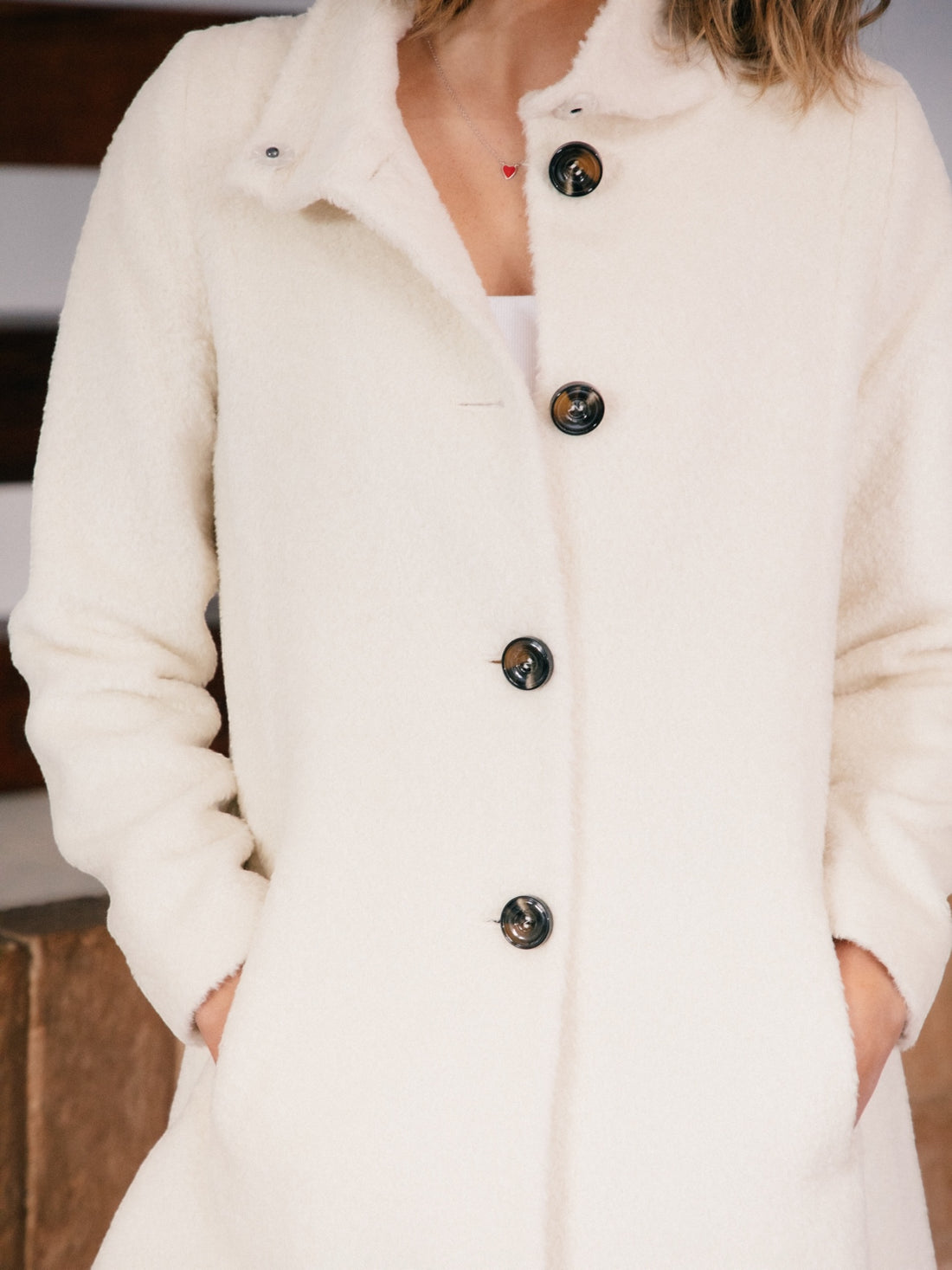 Woman wearing a white alpaca coat with black buttons in an indoor setting.