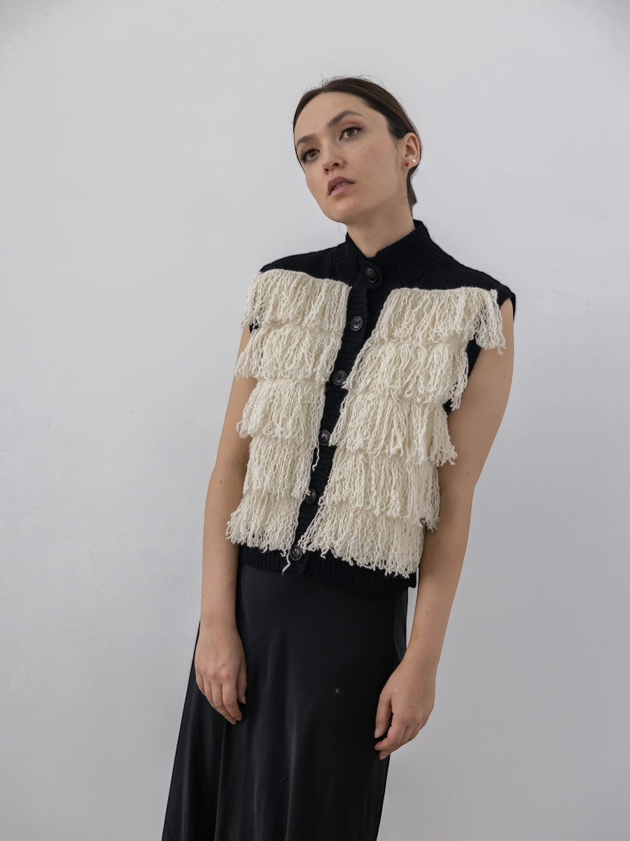 white alpaca fringed button-up vest with black rib, shown on a model against a white background