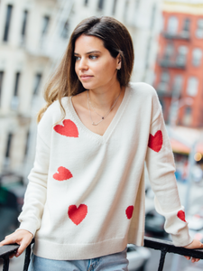 Woman wearing a white knitted sweater decorated with red hearts with blue jeans on a terrace in New York City.
