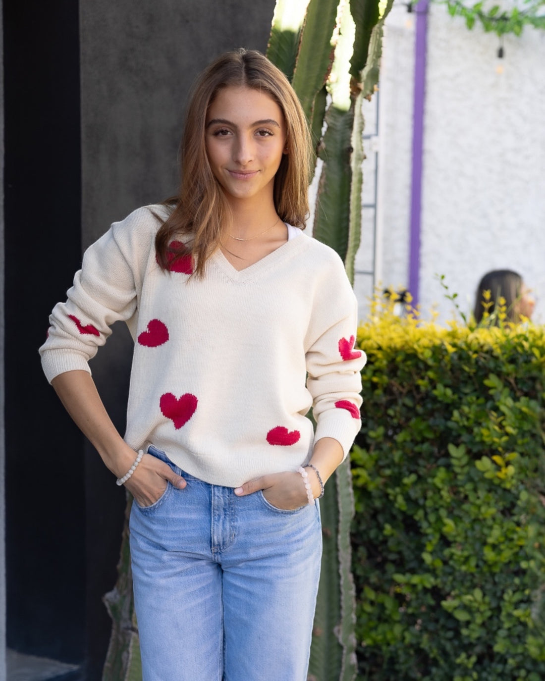 white alpaca sweater with a V-neck and red heart patterns, worn by a model with light blue jeans