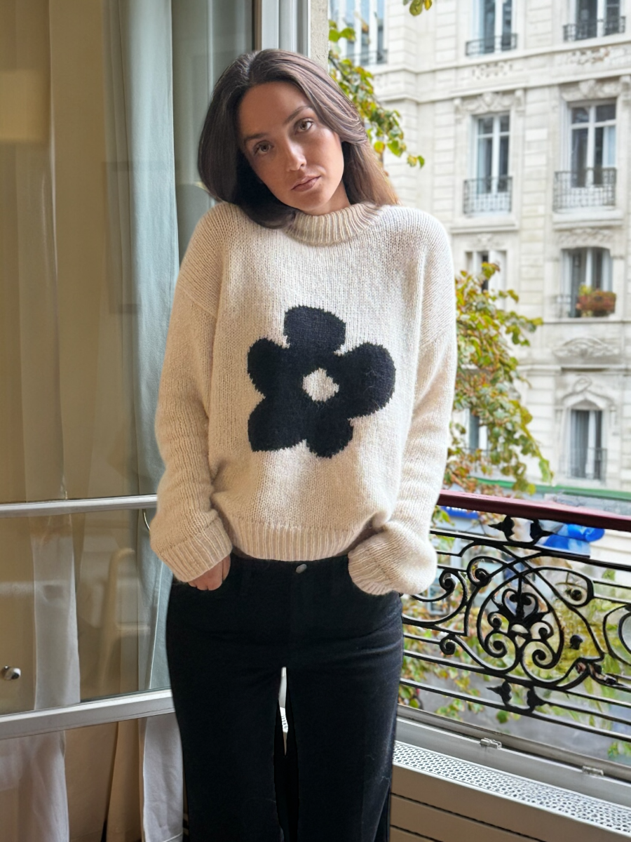 white chunky llama knitted sweater with a large black flower design, worn by a model by a window