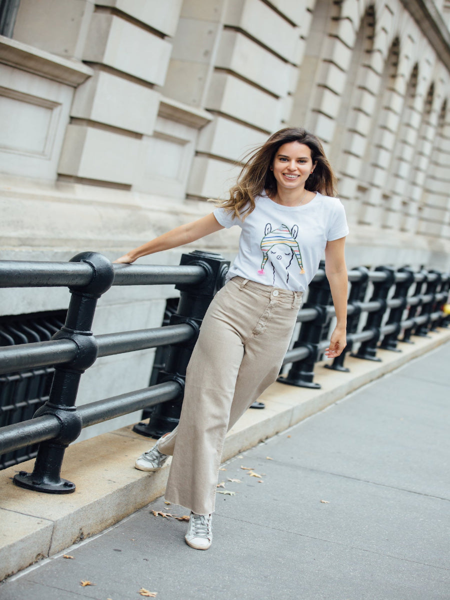 White cotton t-shirt featuring a playful embroidered alpaca motif wearing a colorful striped beanie