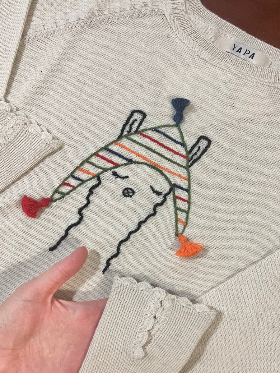 beige alpaca knitted sweater with a llama design wearing a colorful hat, worn by a model in a bridge