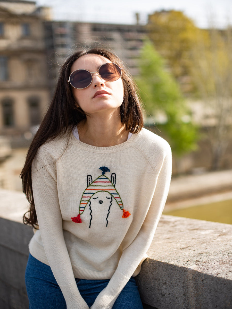 beige alpaca knitted sweater with a llama design wearing a colorful hat, worn by a model in a bridge