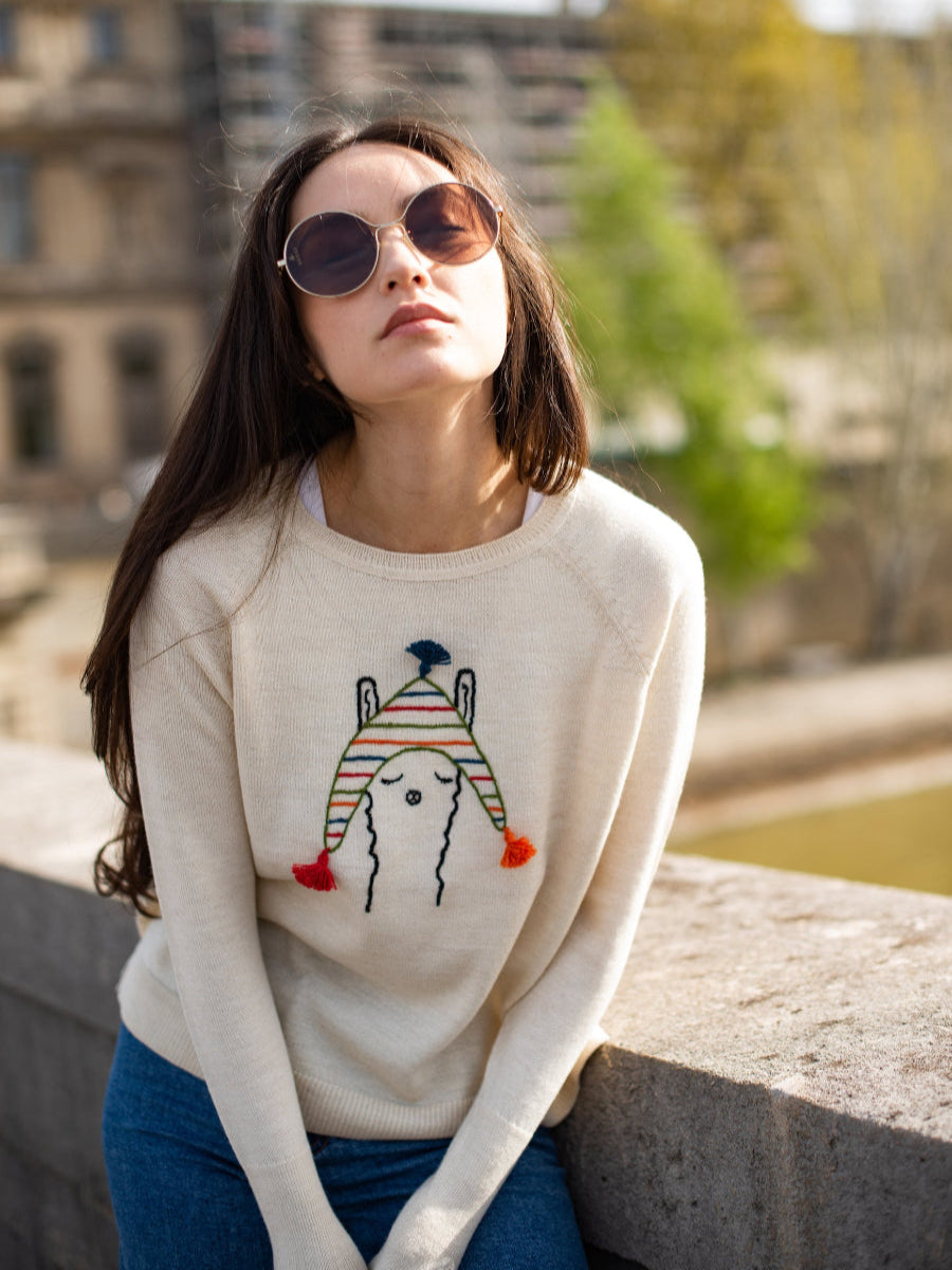beige alpaca knitted sweater with a llama design wearing a colorful hat, worn by a model in a bridge