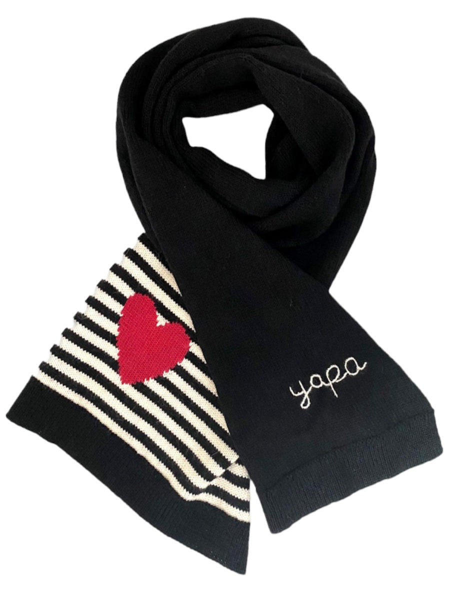 Black alpaca scarf featuring a red heart motif over black-and-white stripes on one end and the word “yapa” embroidered on the other end, shown against a plain background.