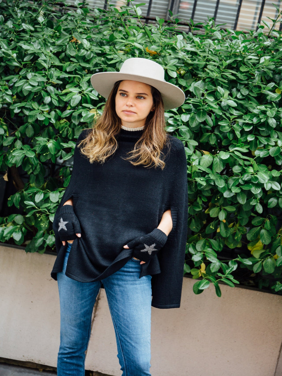 A black alpaca poncho with, worn by a model styled with star-patterned fingerless gloves and a wide-brim hat outdoors