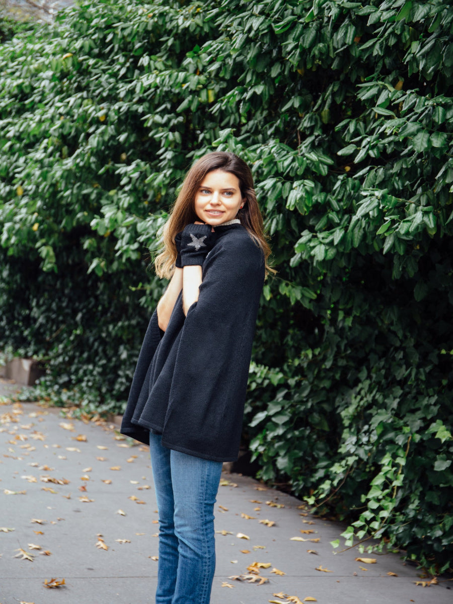 A black alpaca poncho with, worn by a model styled with star-patterned fingerless gloves outdoors