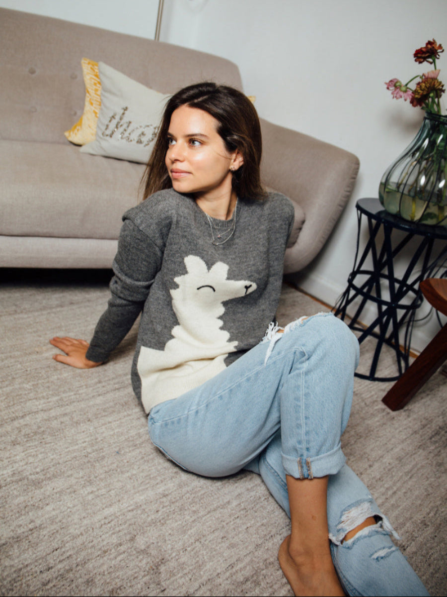 grey alpaca knitted sweater featuring a playful oversized white llama motif on the front, shown here on a model in a relaxed indoor setting.