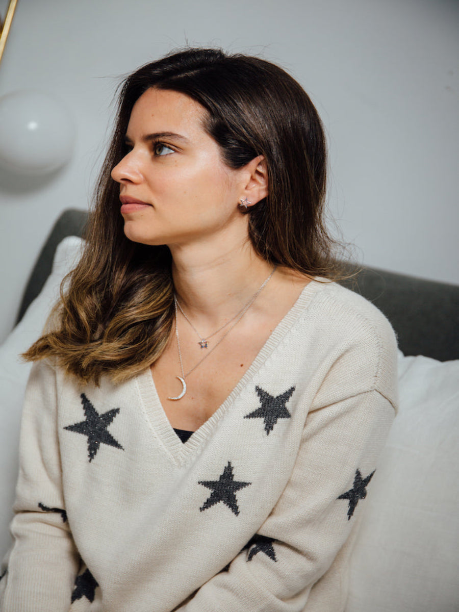 A white alpaca sweater with a V-neck and black star pattern, worn by a model sitting indoors