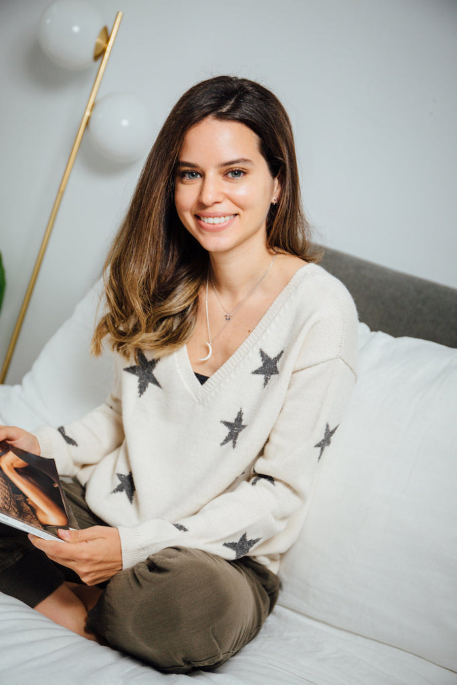 A white alpaca sweater with a V-neck and black star pattern, worn by a model sitting indoors